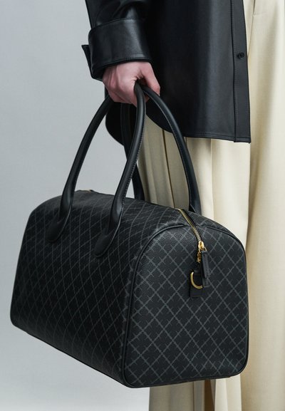 Μαύρη τσάντα duffle με μοτίβο, λεία δερμάτινη υφή, στρογγυλεμένο σχήμα, διπλές λαβές και λεπτομέρεια με χρυστό φερμουάρ, κρατείται από ένα άτομο.