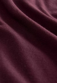 Bordeaux stof met een gladde textuur, die een lichte glans heeft. De weving is strak en benadrukt de rijke kleur en subtiele variaties.