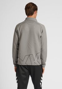 Sudadera de manga larga gris con cuello alzado, que presenta un gran patrón geométrico negro en la parte trasera y un tejido texturizado.