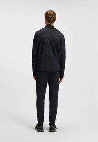 Giacca atletica nera con un motivo testurizzato e pixelato sulla schiena, abbinata a pantaloni neri coordinati e calzature nere.
