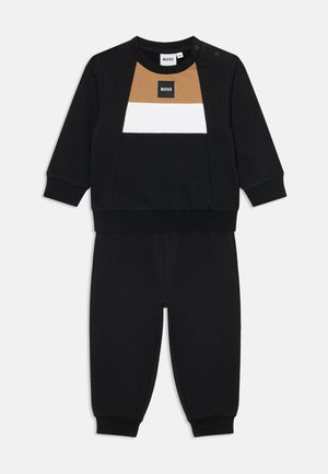 Survêtement noir pour tout-petit avec manches longues, blocs de couleur marron et blanc sur la poitrine, et poignets élastiques aux manches et aux pantalons.