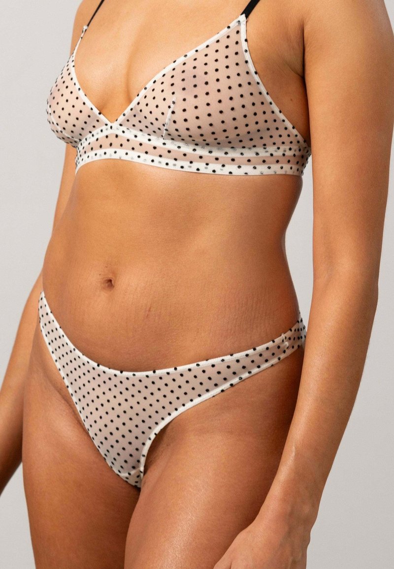 Durchsichtiger, gepunkteter BH und passendes Bikini-Set in Beige mit schwarzen Punkten. Das Set hat ein schlichtes Design mit dünnen Trägern und minimalem Zubehör.