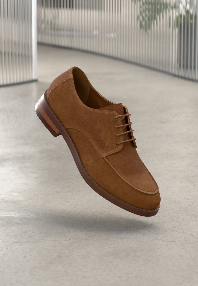 Chaussure de ville en cuir suédé marron avec un bout arrondi, un laçage et un talon en bois. Présente une texture lisse et des détails de coutures subtils.