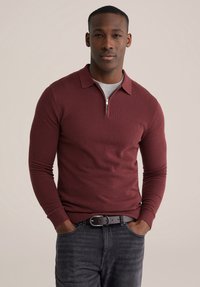 Bordo košulja dugih rukava s patentnim zatvaračem i kragnom, od teksturiranog tkanja. Nošena preko sive majice s okruglim izrezom i uparena s tamnim trapericama.