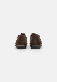 Braune Wildlederschuhe mit flachem Absatz, abgerundetem Zeh und kontrastierender schwarzer Gummisohle. Sie verfügen über eine glatte Textur und ein minimalistisches Design.