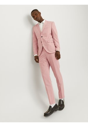 Completo su misura rosa chiaro con giacca a un bottone e pantaloni slim-fit, abbinato a una camicia bianca e mocassini neri.
