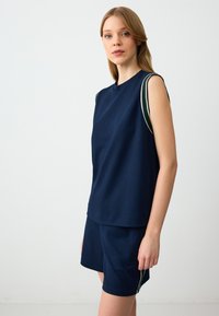 Marineblauwe sportoutfit met een mouwloze top voorzien van groene en witte gestreepte accenten en bijpassende shorts. Soepele textuur en ontspannen pasvorm.