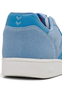 Jasnoniebieskie zamszowe sneakersy z teksturowanymi skórzanymi akcentami, białą gumową podeszwą i wzorzystym detalem na pięcie z dwoma chevronami.