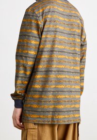 Long-sleeve shirt features horizontal stripes in gray and gold, with a textured appearance and blue cuffs. Detail-oriented design with subtle pattern.