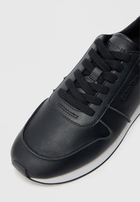 Μαύρο δερμάτινο αθλητικό παπούτσι με στρογγυλή μύτη, δέ�σιμο μπροστά, υφή στην επιφάνεια και διακριτική σήμανση. Διαθέτει λευκή καουτσούκ σόλα.