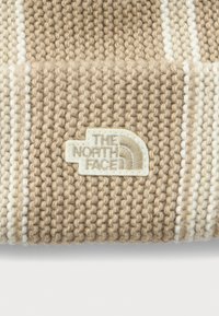 Beige en witte gestreepte gebreide stof met een genaaide rechthoekige beige patch met het "THE NORTH FACE" logo.