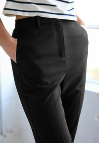Zwarte op maat gemaakte broek met een gladde textuur, zijzakken en een slank ontwerp. Gecombineerd met een gestreept bovenstuk in blauw en wit.