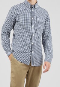 Blue and white checkered button-up shirt with long sleeves, a front pocket, and a classic collar, paired with khaki pants.