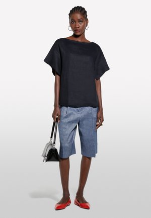 Top in lino nero con vestibilità ampia e maniche larghe, abbinato a pantaloni corti blu fino al ginocchio. Accessoriato con una piccola borsa nera e argento, e ballerine rosse.