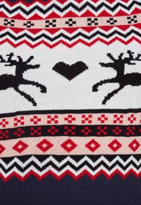 Stickad tröja med ett mönster av renar och hjärtan i svart, rött och vitt. Geometriska detaljer i växlande färger genom hela plagget.