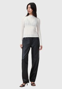 Top bianco trasparente con maniche lunghe e righe verticali, abbinato a pantaloni in pelle nera a vestibilità rilassata e tacchi aperti neri.