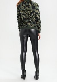 Leggings neri lucidi abbinati a una felpa con motivo camouflage. L'outfit presenta polsini a coste e un design aderente.