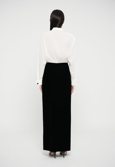 White long-sleeve blouse with a smooth texture, paired with a floor-length black velvet skirt. Features button accents on cuffs.