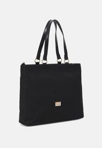 Černá taška přes rameno vyrobená z hladké látky s dvojitými uchy, obdélníkovým tvarem a zlatou kovovou logovkou na přední straně.