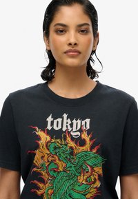 Zwarte katoenen T-shirt met een kleurrijke draakafbeelding in groen en oranje, met de tekst "Tokyo" in een decoratief wit lettertype.
