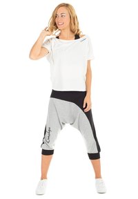 Blusa blanca de manga corta con un ajuste relajado, combinada con pantalones de tiro bajo en gris y negro que cuentan con bolsillos laterales y un detalle de logo.