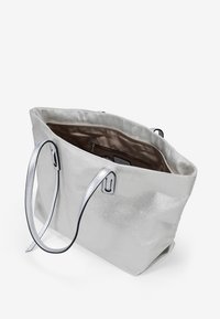 Bolso tote metálico plateado con una superficie texturizada, dos asas en tono plateado y un interior espacioso forrado en tela marrón. Con un bolsillo con cremallera en el interior.