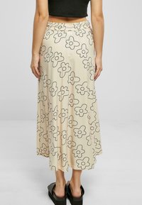 Fustă midi cu model floral în bej, cu flori conturate în negru, având o talie elastică și o siluetă fluidă. Purtați cu pantofi cu talpă platformă negri.
