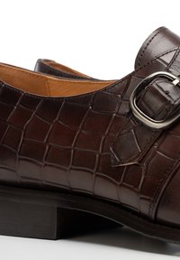 Brauner Lederschuh mit Krokodillederstruktur, verstellbarer Metallschnalle und niedrigem Blockabsatz, innen mit glattem Futter ausgestattet.