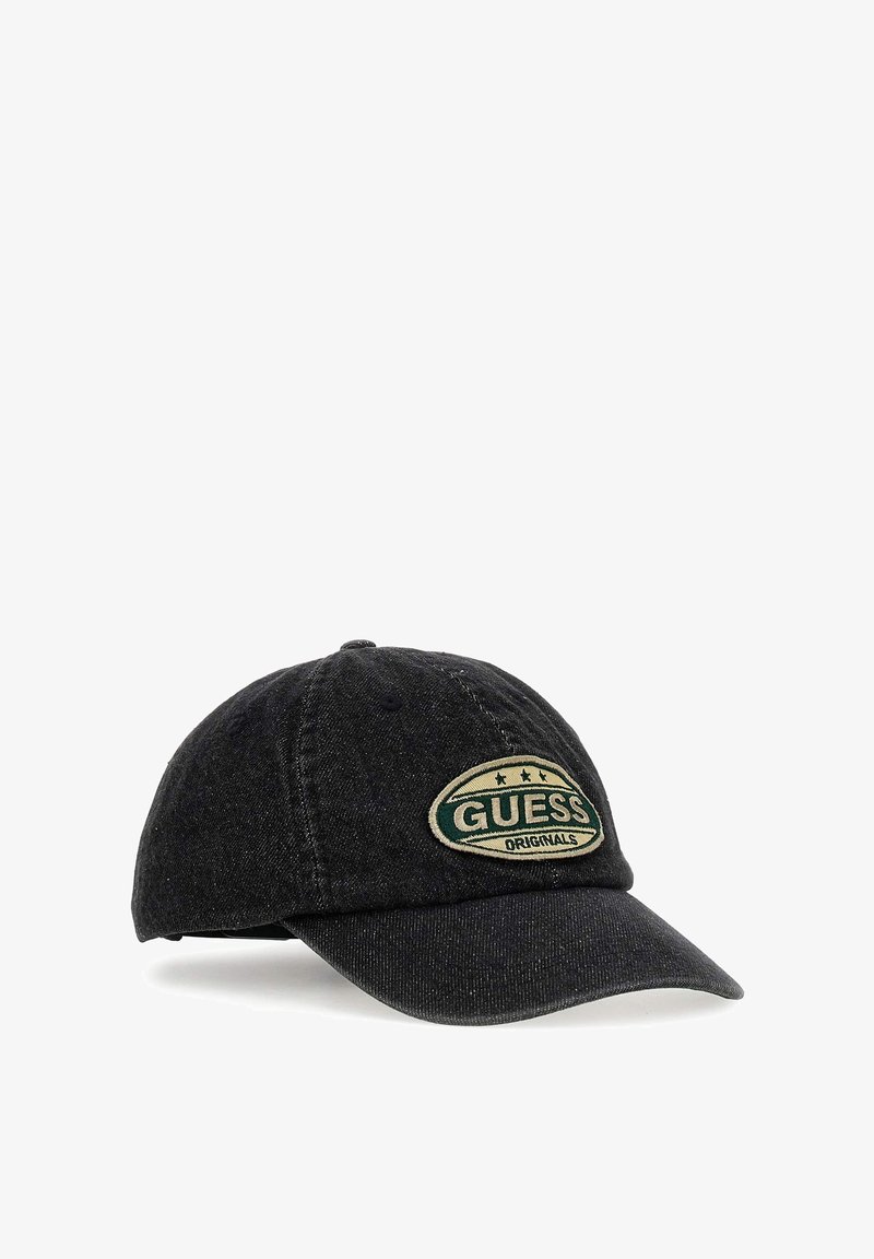 Black denim baseball cap featuring a green and beige "GUESS ORIGINALS" patch with stars, curved visor, and stitched detailing.