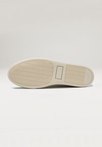 Semelle en caoutchouc beige avec une texture ondulée, un logo moulé et un indicateur de taille. Surface lisse avec des bords arrondis.