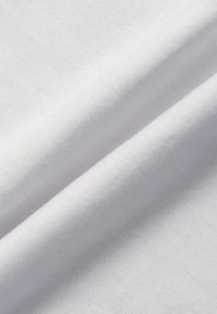 Tissu en coton blanc, texture lisse, superposé, avec des coutures visibles le long des bords, mettant en valeur un éclat subtil et un tombé doux.