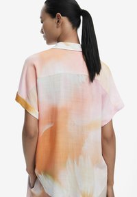 Havnáko s kvetinovým vzorom a krátkym rukávom v jemných pastelových odtieňoch ružovej a oranžovej. Ľahký materiál s voľným strihom a jemnou textúrou.