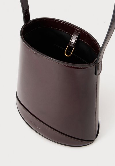 Sac seau en cuir marron foncé avec bandoulière, ouverture en haut montrant un intérieur noir et un petit fermoir doré à l'intérieur.