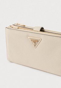 Bézs színű pénztárca texturált anyagból, két cipzáros rekesszel és arany színű, háromszög alakú logóval díszítve.