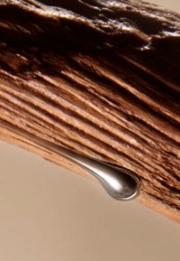 Goccia metallica sospesa su una superficie di legno marrone e texturizzata, che evidenzia la venatura naturale e la finitura del legno.