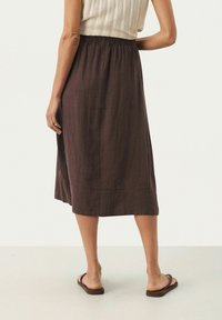 Jupe midi en lin marron avec une taille élastique. L'arrière est lisse avec un ourlet droit. Portée avec des sandales plates marron.