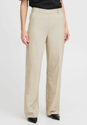 Beige weit geschnittene Hosen mit glatter Textur, taillierter Passform, seitlichen Taschen und formellem Design, kombiniert mit schwarzen spitzen Absätzen.