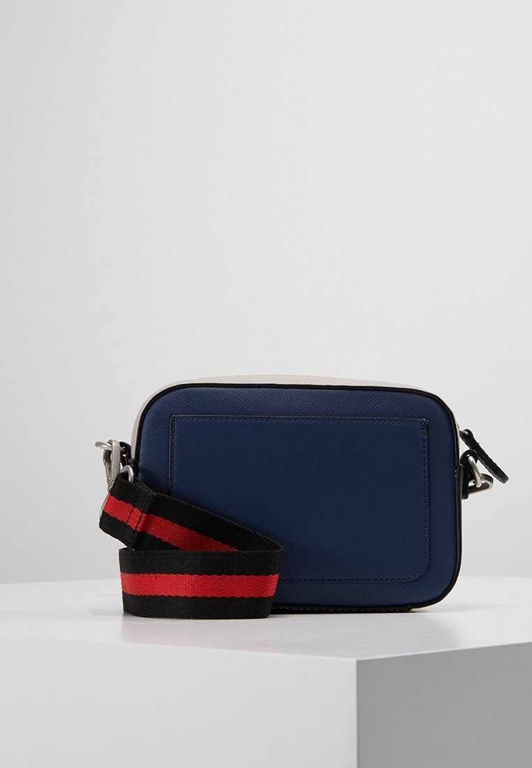 Náměsíčná modrá crossbody taška s texturovaným povrchem, stříbrnými komponenty a černým popruhem se červenými a černými pruhy. Obdélníkový tvar.