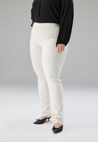 Witte nauwsluitende broek met een gladde textuur en een hoge taille, gecombineerd met zwarte pumps met een spitse neus en strikdetail.