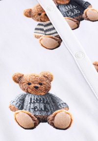 Weißer Stoff mit bunten Teddy-Bären-Illustrationen in Strickpullovern. Ein Bär trägt einen grauen Pullover mit dem Text "little cub".