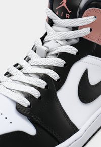 Black and white Nike Air Jordan sneaker with white textured laces, black Nike swoosh, and coral-colored accent near the ankle collar.