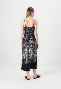 Zwart-witte maxi-jurk met een patroon, dunne spaghettibandjes, vloeiende stof en een licht doorschijnende textuur; voorzien van een uniek abstract ontwerp op de rug.