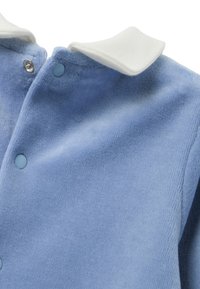 Parte superior de forro polar azul claro y suave con un cuello blanco, que presenta botones a presión y tela texturizada. Vista en primer plano que resalta los materiales.