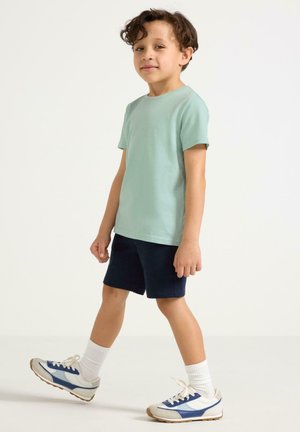 Mintgrön t-shirt med kort ärm, marinblå shorts, vita strumpor och löparskor med blå accenter. Enkelt mönster med avslappnad passform.