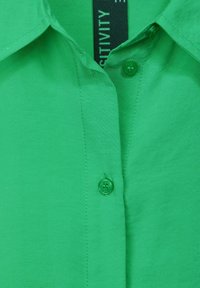 Camicia verde con bottoni, realizzata in un tessuto liscio, dotata di colletto e due bottoni coordinati, con cuciture uniformi.