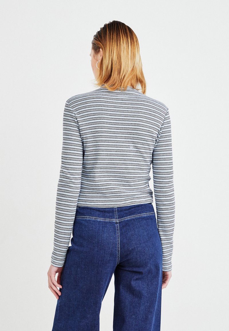 Langärmliges gestreiftes Hemd in Grau und Weiß, kombiniert mit blauen weit geschnittenen Jeans. Das Hemd hat ein figurbetontes Design und einen runden Ausschnitt.