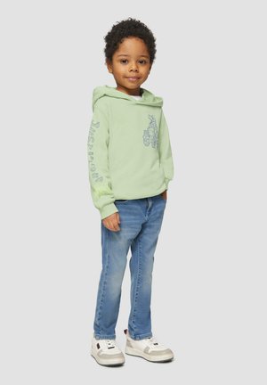 Lichtgroene hoodie met een grafisch ontwerp en tekst op de mouw, gecombineerd met blauwe jeans en witte sneakers. Zachte katoenstructuur.