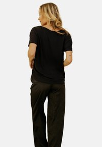 Haut noir à manches courtes avec un col rond et des détails en dentelle sur les épaules, associé à un pantalon large texturé de couleur foncée.