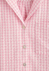 Koszula w różowo-białą kratę z zaokrąglonym kołnierzykiem, pięcioma guzikami i kieszenią na lewej piersi. Wykonana z lekkiego materiału.