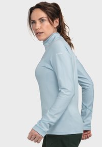 Himmelblaues Langarm-Sportoberteil mit hohem Kragen, gerippter Textur und Daumenlöchern an den Ärmeln; Logo auf der rechten Schulter platziert.